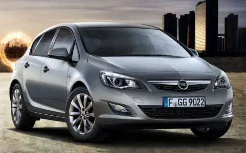 Szary Opel Astra 1.4 Turbo z nowoczesnymi światłami i felgami, na tle miejskiej panoramy i energetycznego kręgu.