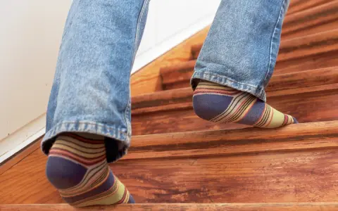 Füße in bunten Socken steigen eine Holztreppe hinauf, die auf eine Renovierung wartet.