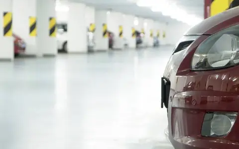 Czerwony samochód na tle rzędu miejsc parkingowych. Zastanawiasz się, ile miejsc parkingowych na mieszkanie jest dostępne?