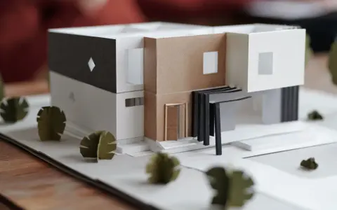 Maquette d'une maison individuelle moderne aux lignes épurées, avec des éléments en carton et des arbres stylisés.