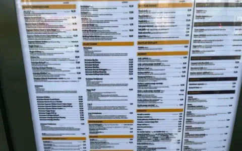 Menu McDonald's z ofertą promocyjną i klasyczną. Widoczne są ceny i nazwy produktów, np. McWrap, McRoyal, Lody z polewą mango-marakaja. Opłata reklamowa jest tu widoczna w postaci prezentacji oferty.