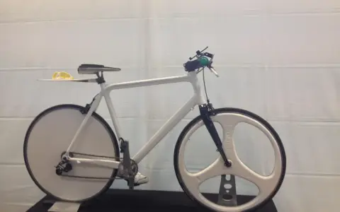 A sleek, white 3d printed bike with unique disc and tri-spoke wheels. Yellow sunglasses rest on the seat.