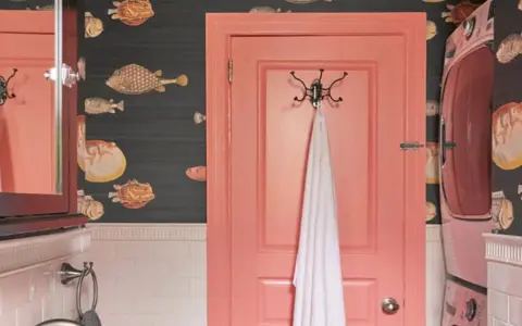 Un baño con papel tapiz de peces y **puertas de dos colores**: una rosa coral y otra de madera oscura con espejo.