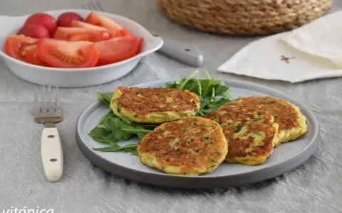 Tortitas de calabacín doradas y esponjosas, servidas sobre rúcula fresca. Acompañadas de una ensalada de tomate y rábano.