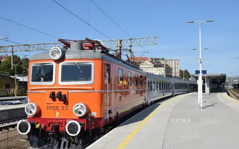 Pomarańczowa lokomotywa EP05-23, znana jako "eic chrobry", stoi na stacji. Pociąg jest gotowy do podróży.