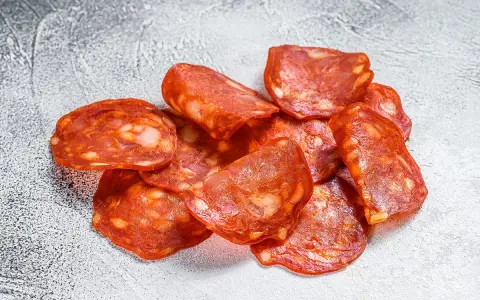 Plasterki pikantnego chorizo, wędzonej kiełbasy wieprzowej, z widocznymi kawałkami tłuszczu.