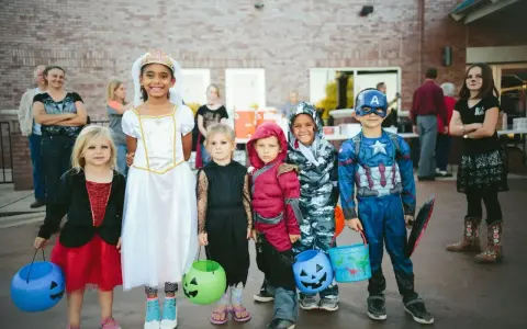 Dzieci w strojach na Halloween, gotowe na psikusy i zbieranie słodyczy. Wśród nich księżniczka, Kapitan Ameryka i inne postacie.
