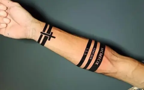 Czarny tatuaż pasek na przedramieniu z krzyżem, napisem "CONTINUE", "1..2..3." i rzymską liczbą MCMXCIX.