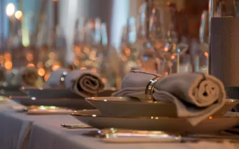 Ett elegant dukat bord med rullade servetter, hållna av en gyllene organza band-liknande ring. Mjuk belysning skapar en varm atmosfär.