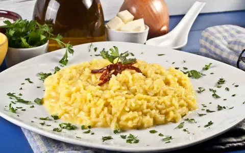Aksamitne risotto alla milanese, ozdobione suszonymi papryczkami i natką pietruszki, prezentuje się apetycznie na białym talerzu.
