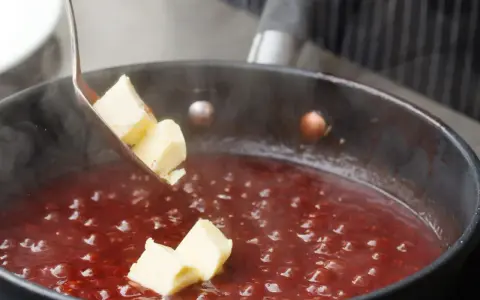 Butterstücke werden in eine köchelnde rote Sauce gegeben, um sie zu **saucen andicken** und zu verfeinern.