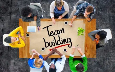Un groupe diversifié autour d'une table discute de "team building". Ils collaborent, partageant des idées pour renforcer leur unité.