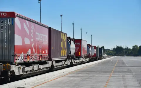 Długi pociąg towarowy z kontenerami, w tym czerwonymi z logo COSCO i żółtymi, czeka na dalszy transport kolejowy.