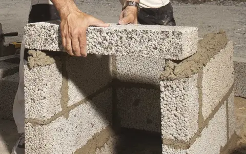 Byggare lägger mura lecablock på betongplatta. Murbruket syns mellan blocken.