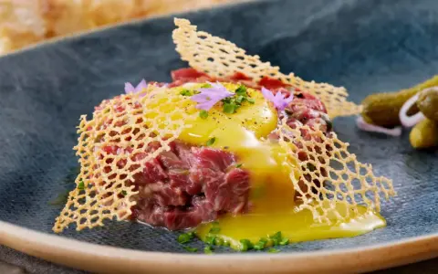 Delicioso steak tartar con huevo crudo, crujiente de queso y pepinillos. Una receta para disfrutar.