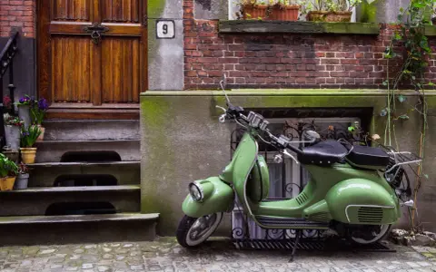 Zielony skuter, klasyk, czeka na właściciela. Parkowanie motocykla na chodniku przed drzwiami z numerem 9.