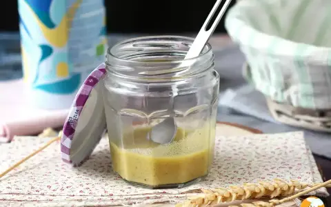 Un bocal de vinaigrette maison, prêt à assaisonner une salade fraîche. Une cuillère repose dans le mélange jaune pâle.