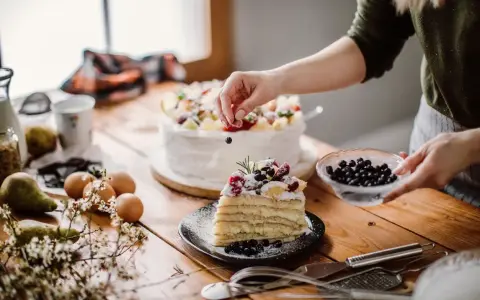 Manos expertas decoran un pastel en una mesa de reposteria y pasteleria, con frutas frescas y arándanos.
