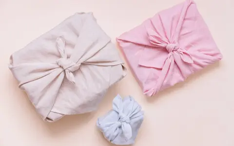 Trois paquets cadeaux joliment emballés dans des tissus de différentes couleurs (beige, rose, bleu clair). Lequel tissu pour furoshiki ? Le lin semble idéal.