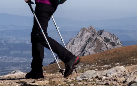 Wybierając jakie końcówki do kijków w góry, pamiętaj o stabilności. Widok na górzysty krajobraz z turystą używającym kijków trekkingowych.