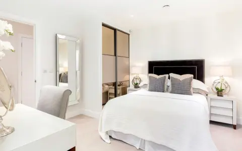 Elegante camera da letto senza finestra, con letto bianco, specchio a figura intera e un angolo toeletta.