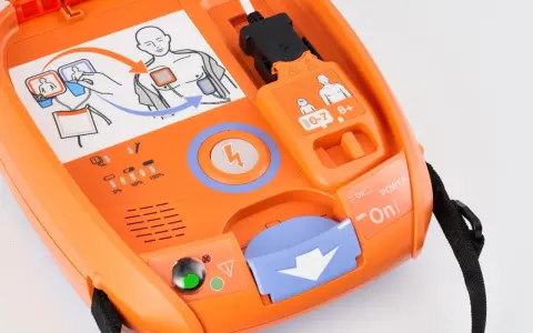 Pomarańczowy defibrylator AED z instrukcją użycia i wskaźnikami.