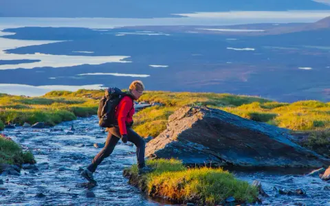 Vandrare korsar en bäck i Abisko, med Kebnekaise-massivet i bakgrunden.