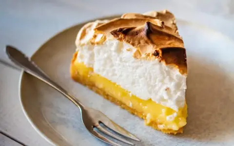 Rebanada de lemon pie con merengue dorado y relleno cremoso, lista para ser disfrutada con un tenedor.