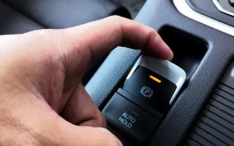 Dłoń naciska przycisk elektrycznego hamulca postojowego. Pomoc w zrozumieniu, jak wyłączyć elektryczny hamulec postojowy.
