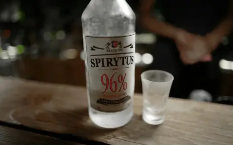 Spirytus 96% – alkohol, który ma najwięcej procent. Butelka i kieliszek na drewnianym blacie.