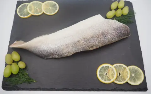Filet ryby na czarnej desce z plasterkami cytryny, winogronami i koperkiem.