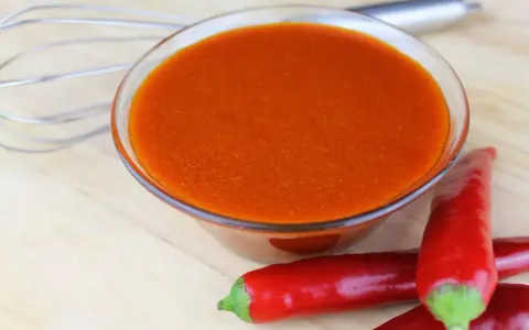 Schüssel mit leuchtend orangeroter Buffalo Sauce, daneben rote Chilis und ein Schneebesen. Perfekt für Flügel!