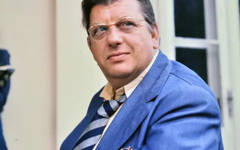 Portret Mariusza Dmochowskiego w okularach i niebieskiej marynarce. W tle okno.
