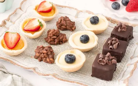 Bandeja con variedad de petit fours: tartaletas de fresa y arándano, bombones de chocolate y dulces de frutos secos.
