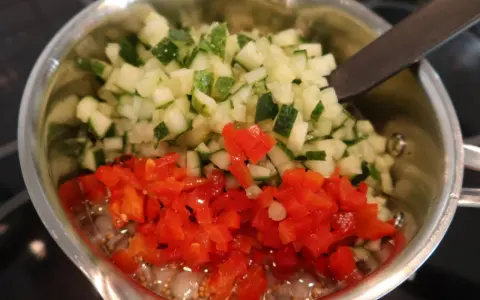 Finhackad gurka och röd paprika i en kastrull, redo för ett bostongurka recept. En sked vilar i blandningen.