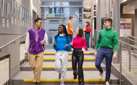Studenci na schodach w nowoczesnym budynku Uniwersytetu Dolnośląskiego.