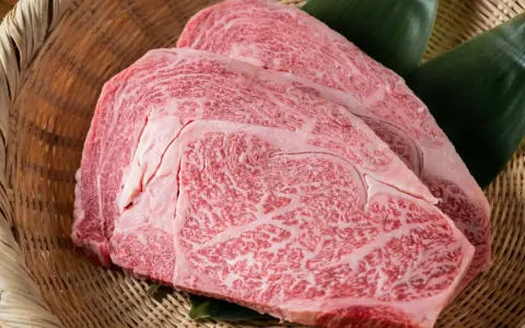 Dos cortes de carne japonesa cara, con marmoleado intenso, reposan sobre hojas verdes en una cesta de mimbre.