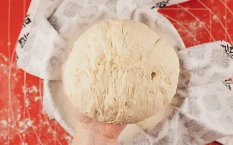 Masa de pan de patata esponjosa, lista para hornear, cubierta con un paño decorado.