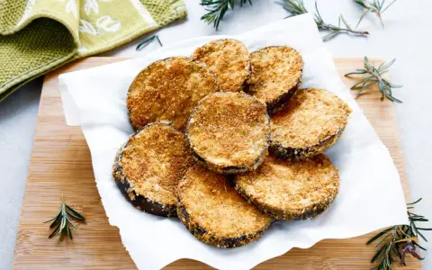 Cotolette di melanzane dorate e croccanti, servite su carta bianca con rametti di rosmarino.