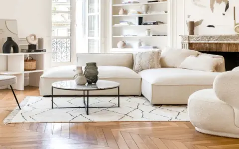 Un soggiorno luminoso con divani e design moderno. Un divano componibile bianco, una poltrona bouclé e una sedia grigia su un tappeto geometrico.