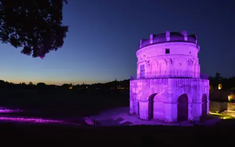 Torre antica illuminata di viola in una magica pink night. L'erba e gli alberi riflettono la luce, creando un'atmosfera surreale.