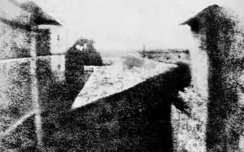Dagerotypia przedstawiająca widok z okna, z widocznymi dachami i sylwetką człowieka.