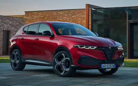 Czerwone Alfa Romeo Tonale na tle nowoczesnej architektury. Sprawdź aktualną alfa romeo tonale cena i konfigurację.