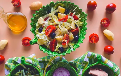 Un'insalata di patate napoletana colorata con pomodorini, olive e lattuga, servita in una ciotola a forma di foglia.