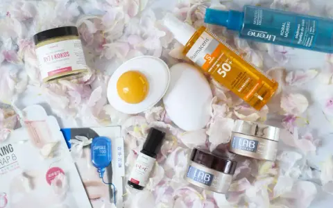 Kosmetyki do pielęgnacji: kremy, serum, mgiełka do ciała, olejek ochronny i peeling ryżowy. Całość ułożona na płatkach kwiatów, tworząc wiosenny, roc.