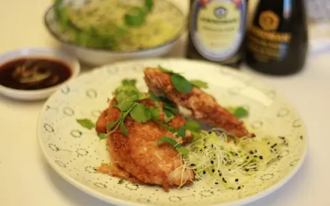 Crujiente solomillo de pollo empanado, adornado con cilantro fresco y brotes, servido con salsa y un cuenco de ensalada.
