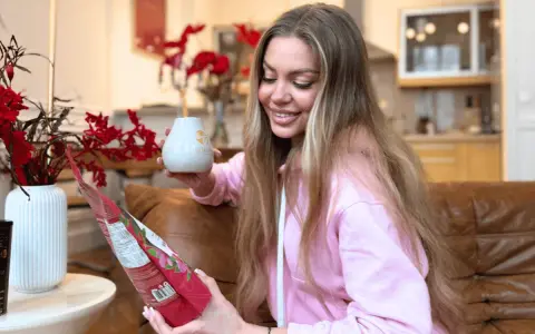 Uśmiechnięta kobieta trzyma kubek i paczkę yerba mate, przygotowując się do parzenia.