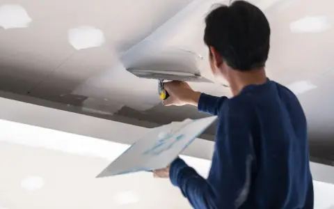 Un trabajador aplica masilla al techo, resolviendo la duda de si que se pinta primero el techo o las paredes.