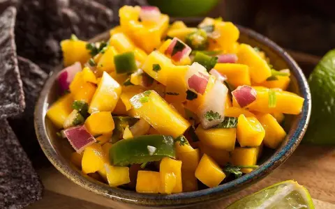 En skål med färgglad mango salsa, med tärnad mango, rödlök, grön paprika och koriander. Serveras med tortillachips och limeklyftor.