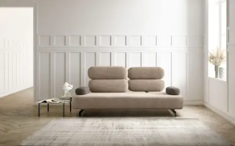 Un elegante divano beige, un'opera d'arte di design, domina la scena. Accanto, un tavolino con libri e una scultura moderna.